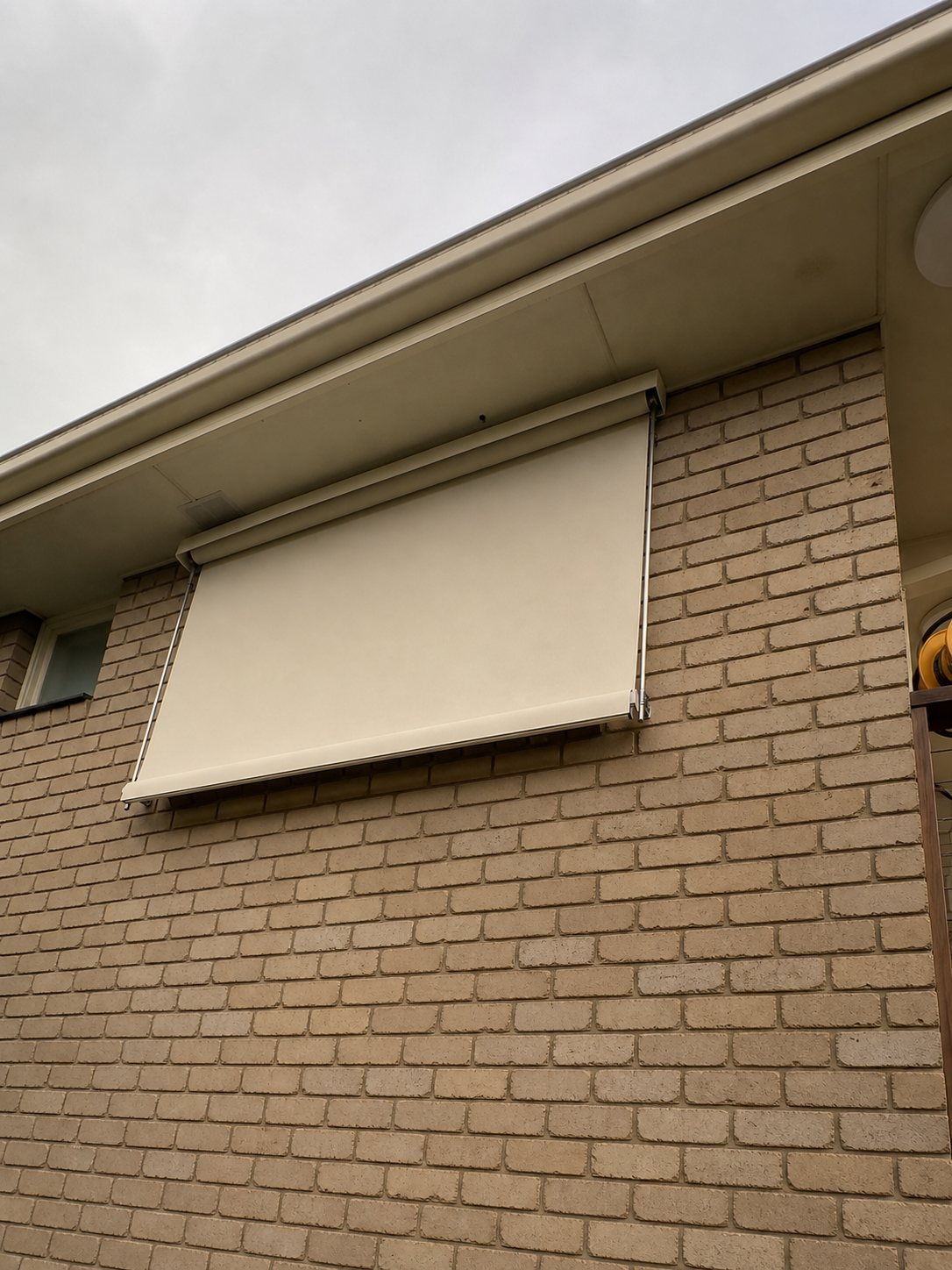 Cream fixed guide awning fitted on a brick wall